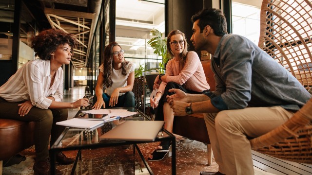 Four people are seated at a table having a casual business meeting.