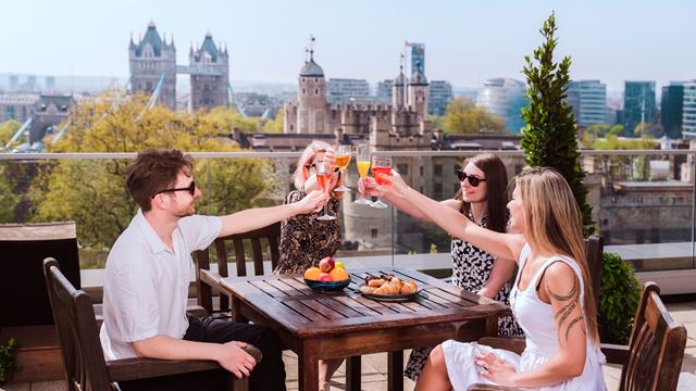 Unique experiences in London include rooftop drinks overlooking the iconic Tower of London and Tower Bridge. Credit: Antoine Buchet. Image courtesy of London & Partners. Three friends enjoying drinks on a London rooftop in summer with views of Tower Bridge and the Tower of London in the background.