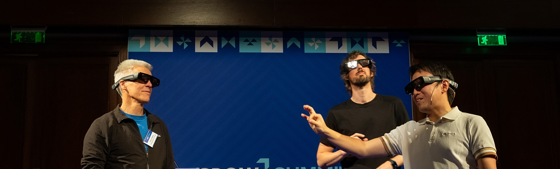 Three men wearing virtual reality glasses on a stage at a technology conference.