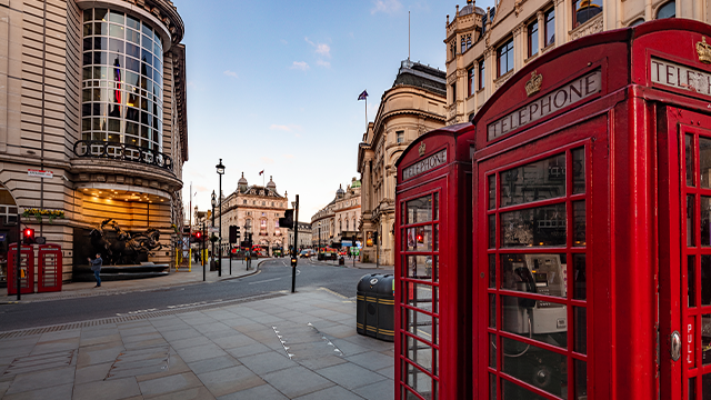 A closeup of two red telephone boxes and Piccadilly Circus in the background