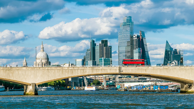 A daytime view of the City of London and St Paul's Cathedral, with a bridge over the river Thames in the foreground. A red double decker bus is crossing the bridge.