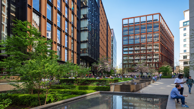A daytime view of a modern green area with water features surrounded by modern office buildings.