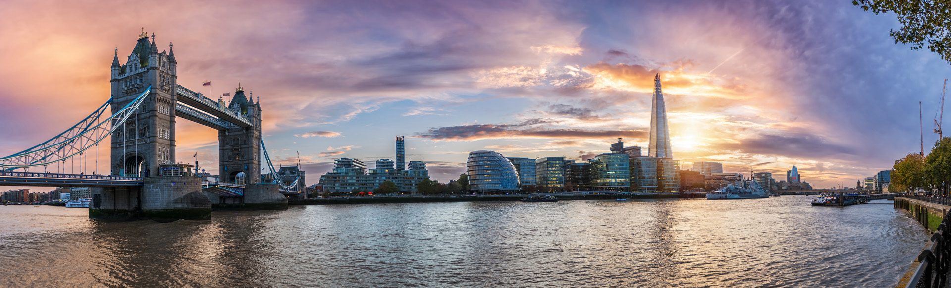 A wide angle view of the river Thames at sunset, with Tower Bridge and The Shard in the background. 