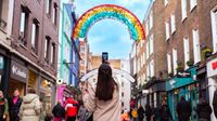 A person stands on Carnaby Street and takes a picture of a rainbow arch on their smartphone