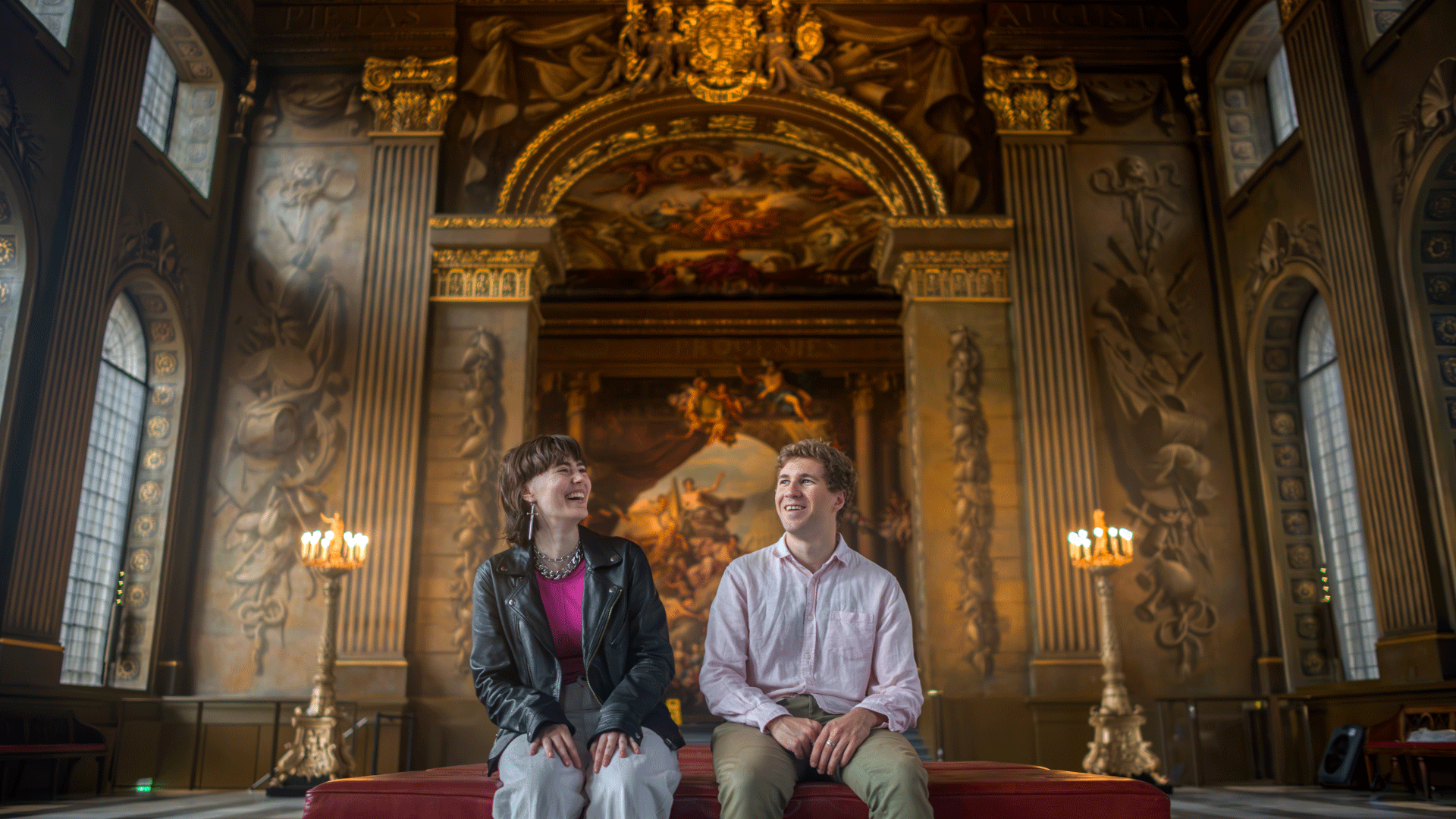 Two people look up at the painted hall in Greenwich with its intricate details and candles in the corner of the room