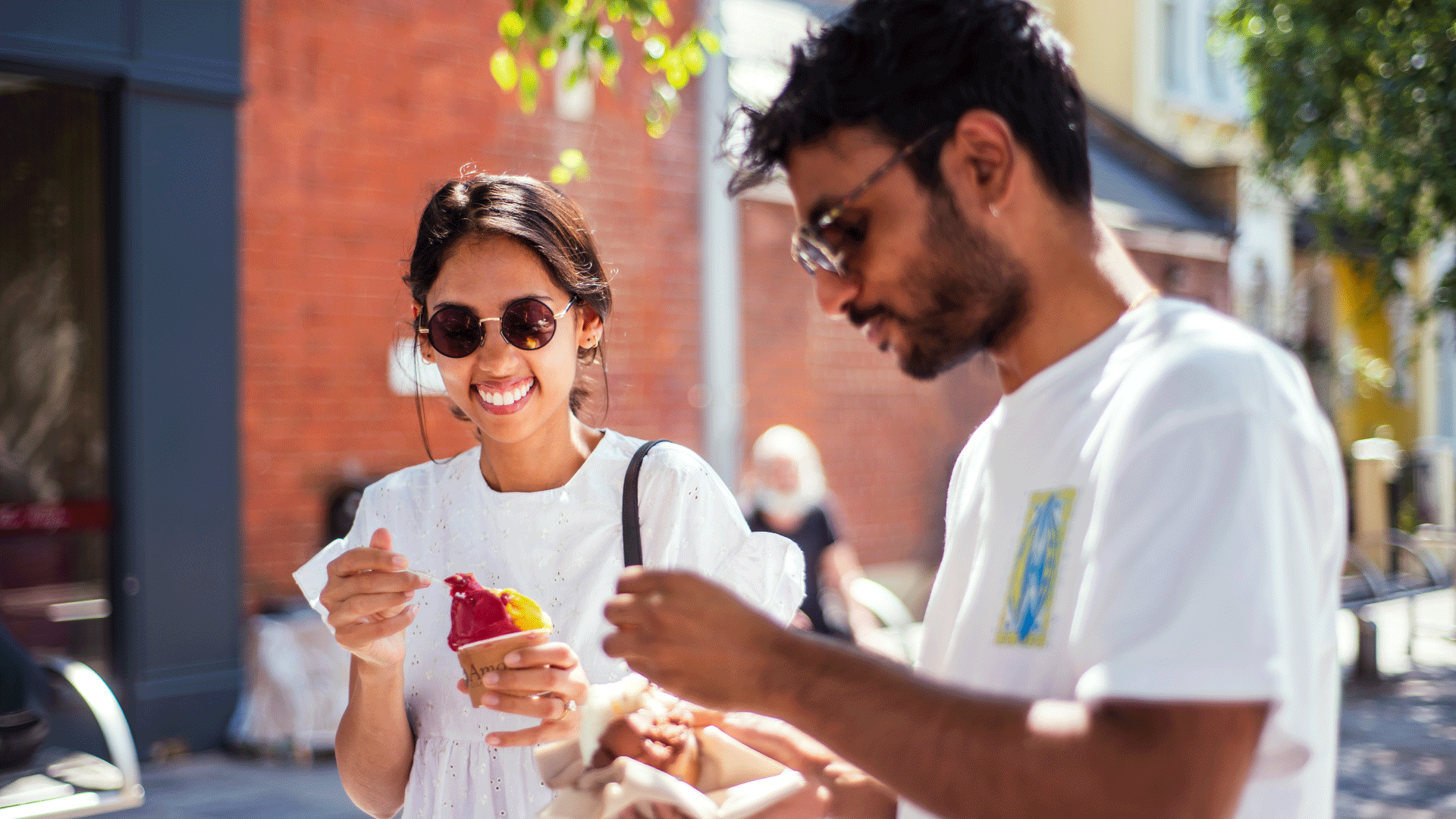 Two friends enjoy ice creams together in the sunshine at a London market